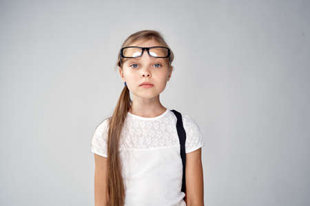 serious girl schoolgirl with glasses looking at the camera on a gray background.の写真素材