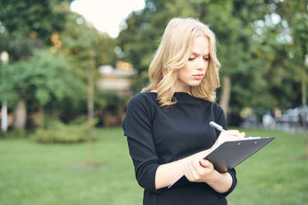 blonde in a black dress makes notes in a notebook.の写真素材