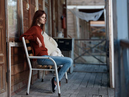 A girl on a bench in a red sweater in the background of a cottage.の写真素材