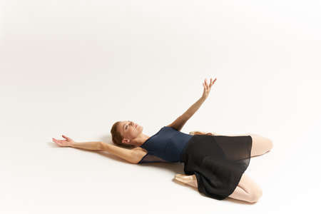 The ballerina lies on the floor and pulls her hand upwards.の写真素材