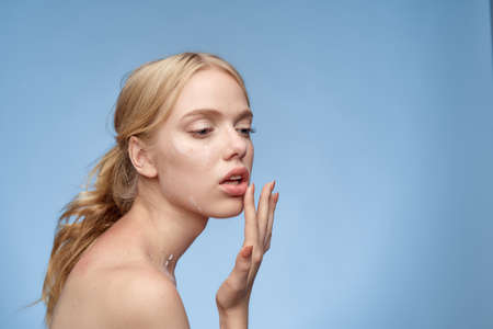 young girl is applying lipstick on a light blue background.の写真素材