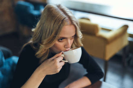 blonde in a cafe drinking from mugs.の写真素材