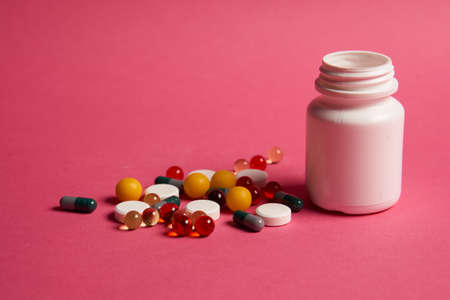 white jar and colored pills on a pink background.