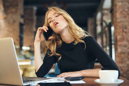 blonde in a cafe talking on the phone with a laptop and coffee.の写真素材
