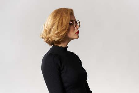 Blonde with glasses and a black sweater on a light blue background.の写真素材