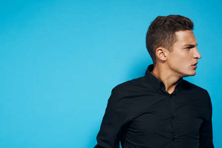 man in a black shirt on a blue background looking away.の写真素材