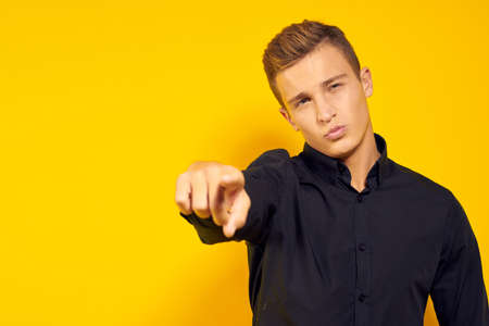 man in a black shirt on a yellow background points a finger at you.の写真素材