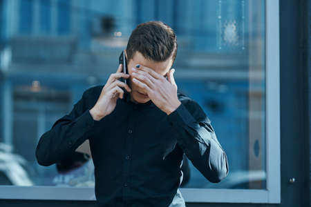 man talking on the phone and covering his face with his hand.の写真素材