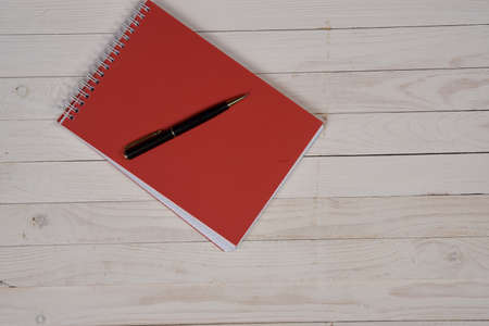 wooden background, red notebook, black pen.の写真素材