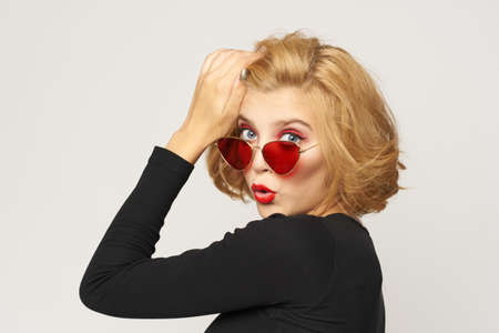 Blonde in red glasses, with a hand near her face fooling around.