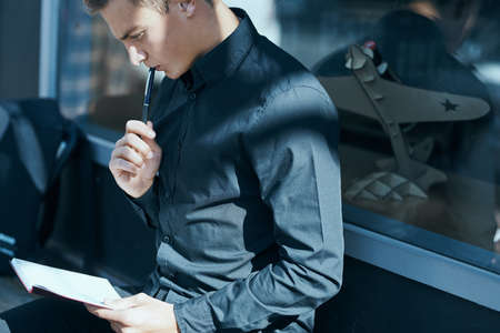 A man holds a pen in his mouth, thinking about an exercise book.