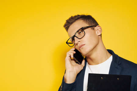 portrait of a business man wearing glasses talking on the phone on a yellow background.の写真素材