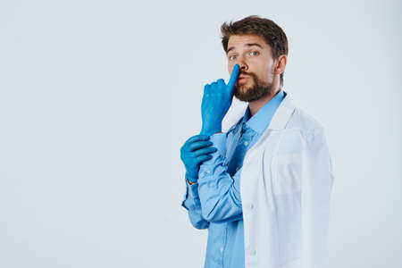 A man with a beard on a light background in a medical dressing gown, emotions, a doctor, medicine, rubber gloves, empty space for copying.の写真素材