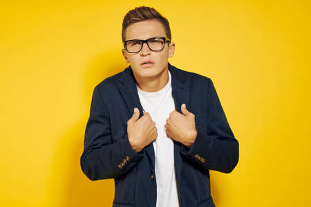 a man in glasses holds on to a jacket on a yellow background.の写真素材