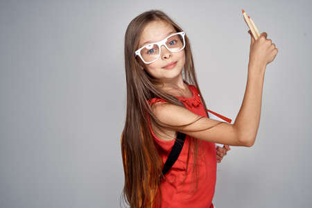 little girl in white glasses holds pencils on black background.の写真素材