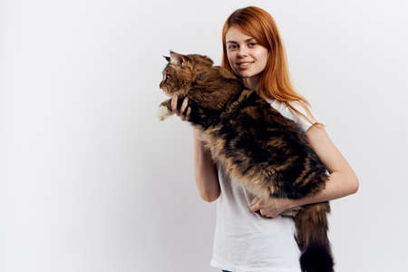 red-haired woman holding a fluffy cat, light background.の写真素材