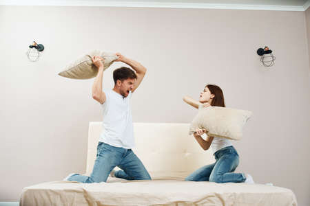 A man and a woman are fighting pillows on the bed and indoorsの写真素材