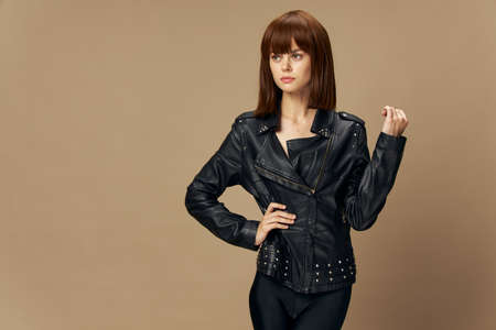Young beautiful woman posing on a beige background in the studio in a black leather jacket