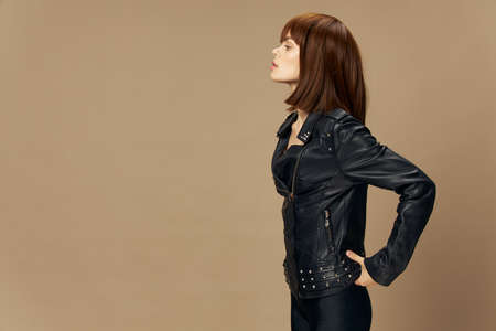Young beautiful woman posing on a beige background in the studio in a black leather jacket