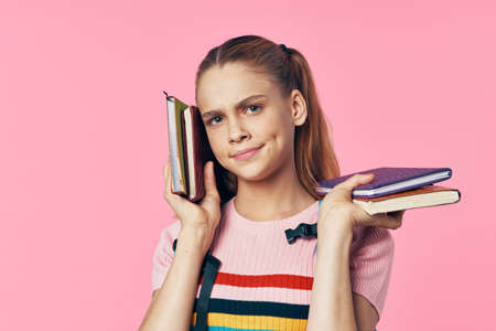 A smart schoolgirl with books in her hands on a pink background