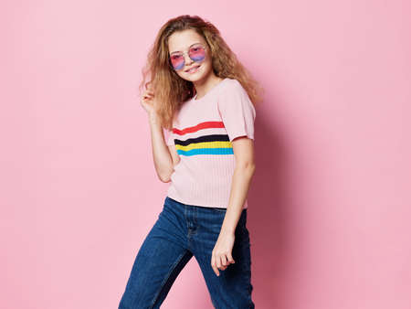 Happy girl in glasses on a pink background her jeans t-shirt