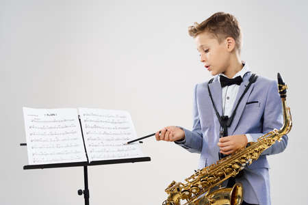 A boy in a classic suit with a saxophone considers notesの写真素材