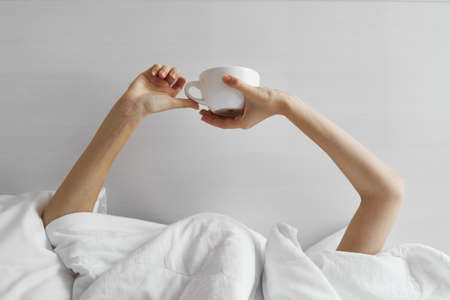 white mug in female hands and a blanket, bed room