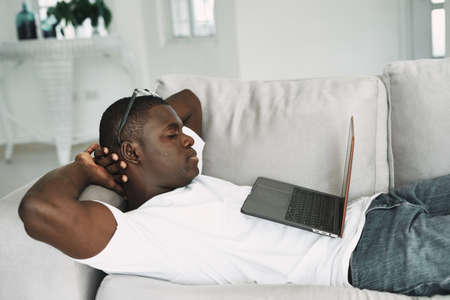A guy of African appearance on the couch with a laptop