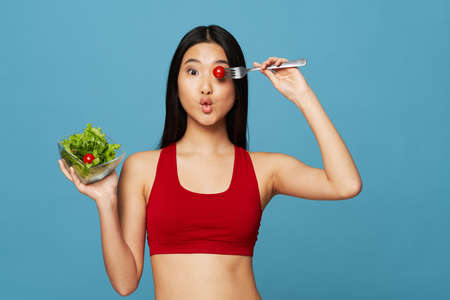 Slender woman with a plate of salad in hand and a tomato on a forkの写真素材