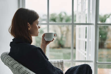 woman in a chair with a cup of coffee looking out the windowの写真素材