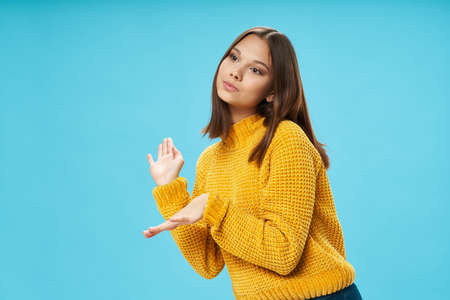girl in a yellow sweater on a blue background gesturing with her handsの写真素材