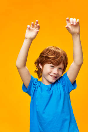 child raised hands redhead boy blue t-shirt yellow backgroundの写真素材