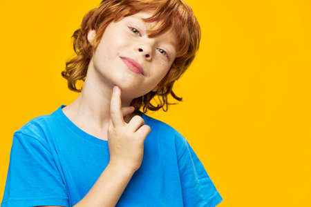 Portrait of a child redhead boy close-up blue t-shirt yellow background