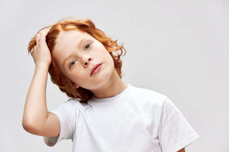 A teenager with red hair holds a hand on his head white T-shirt
