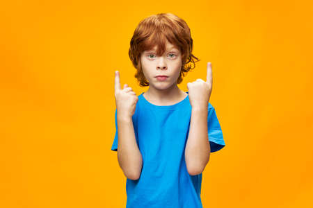 A red-haired boy in a blue T-shirt shows a free space with a thumb up