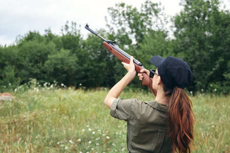 Military woman holding a gun aiming hunting green leaves