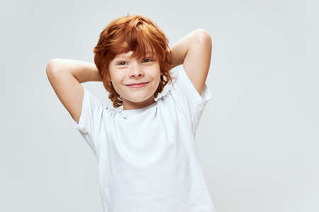 Red-haired boy holds hands behind his head smile white t-shirt studioの写真素材