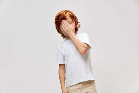 Red-haired boy mortgage near face in white t-shirt gray background
