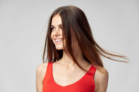 A joyful brunette woman in a red T-shirt turned her head to the side on a light background