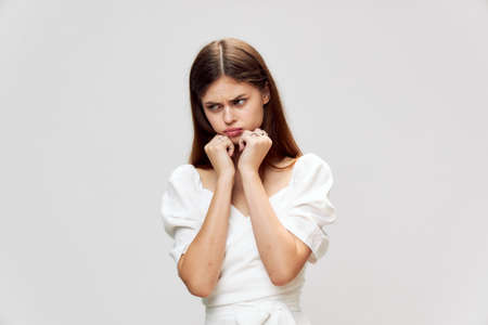 Sad woman looks away from her hands near her face displeased white t-shirt