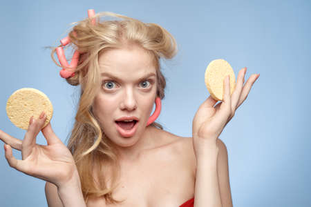 A blonde with bare shoulders holds cotton pads near her face skin care light background