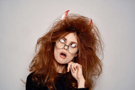 Brunette in a devil costume on Halloween red horns glasses black dress
