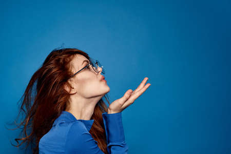Energetic red-haired woman in blue shirt with glasses gesturing with handsの写真素材