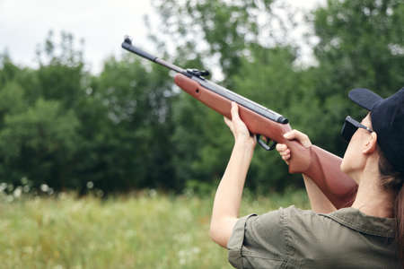 Woman on nature Aiming upward with a hunting rifle, rear view green overalls
