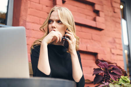 woman working for laptop in a cafe on the street near a brick building freelancer