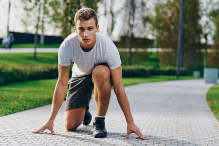 Athletic man in shorts and a t-shirt prepares for jogging in nature in the park near the trees on...