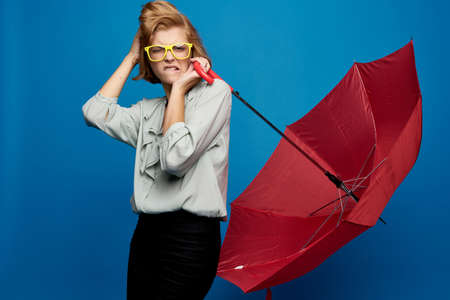 A woman with a red umbrella on a blue in a light shirt and yellow glassesの写真素材
