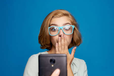 A woman with a red umbrella on a blue background in a light shirt and yellow glassesの写真素材