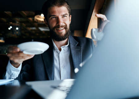Business man sitting in a cafe with a cup of coffee in his hands in front of a laptop technology communicationの写真素材