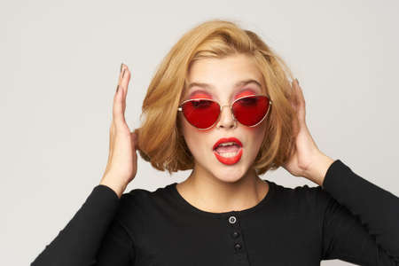 Blonde with short hair in sunglasses black jacket cropped view light background